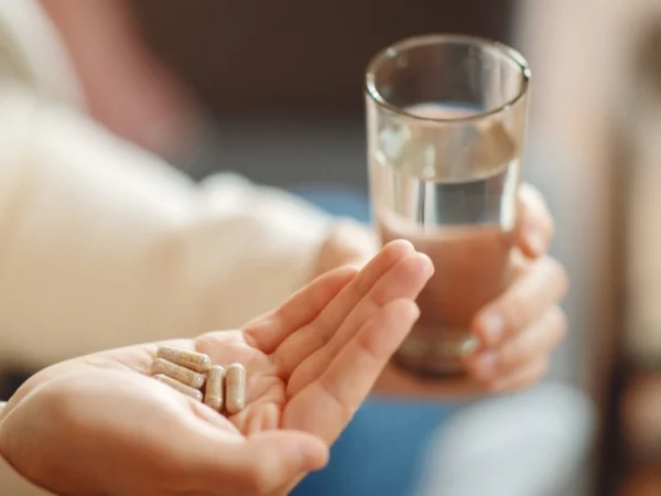 Person holding supplement capsules in one hand and a glass of water in the other