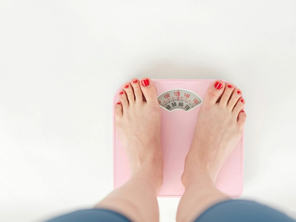 Person standing barefoot on a pink bathroom scale