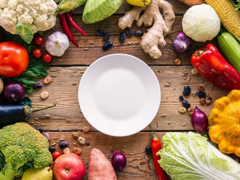 Flat lay, vegetables on a wooden background and an empty white plate.