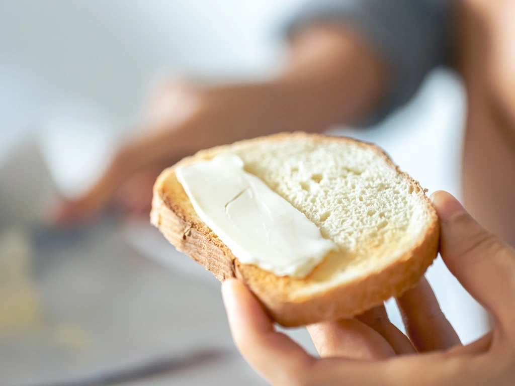 Person holding a slice of white bread with butter