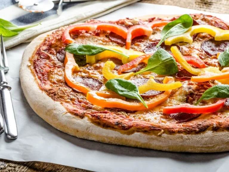 Whole pizza topped with bell peppers, pepperoni, and spinach leaves