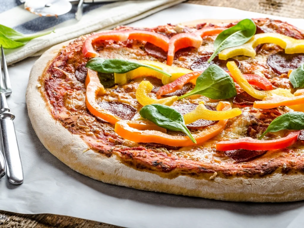 Whole pizza topped with bell peppers, pepperoni, and spinach leaves