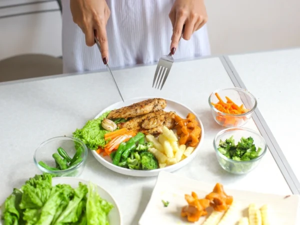 A woman holding a knife and fork, with a balanced meal in front of her