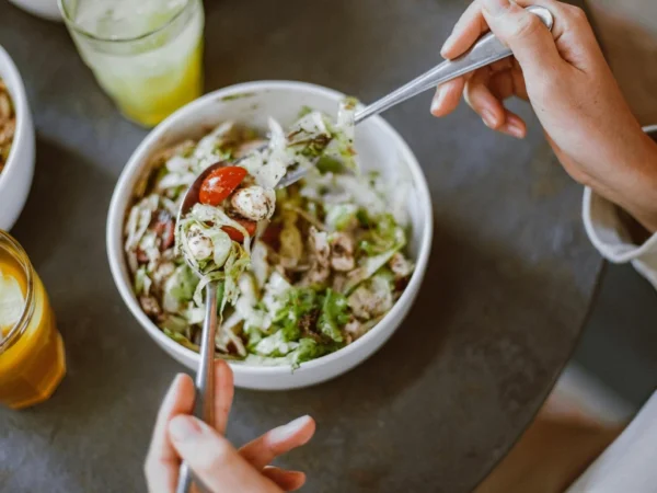 Person eating a fresh salad with lettuce, cherry tomatoes, and chicken in a bowl at a dining table