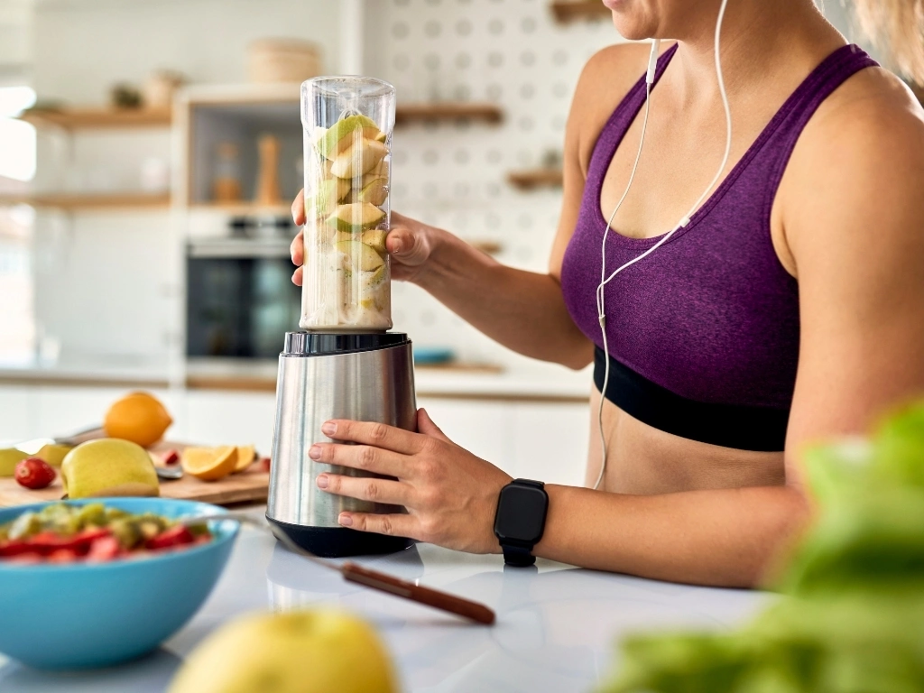 Woman in sportswear blending fruit smoothie, while listening to music