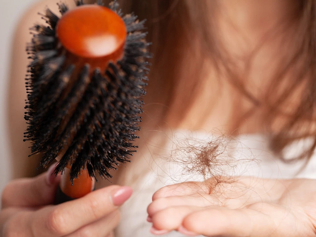 A woman holding a brush and loose strands of hair