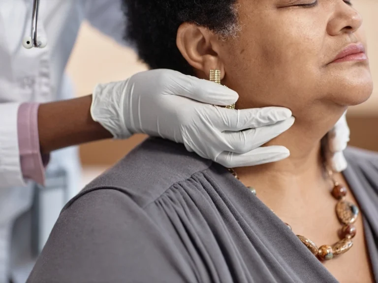Healthcare professional wearing gloves examining a woman’s neck to assess the thyroid gland