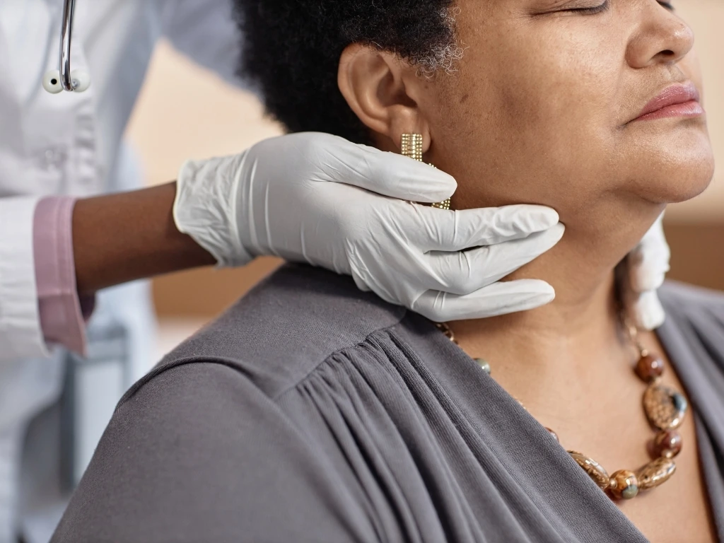 Healthcare professional wearing gloves examining a woman’s neck to assess the thyroid gland