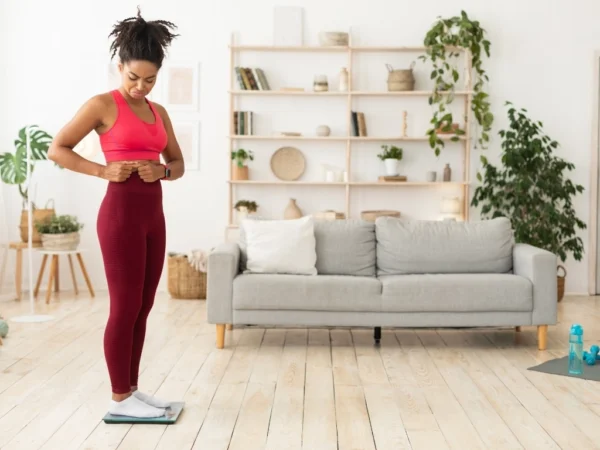 Sad Black Girl Touching Belly Standing On Scales At Home