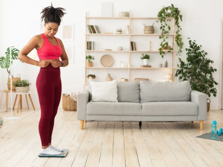 Sad Black Girl Touching Belly Standing On Scales At Home