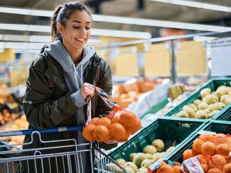 Happy woman buying oranges in plastic mesh at supermarket