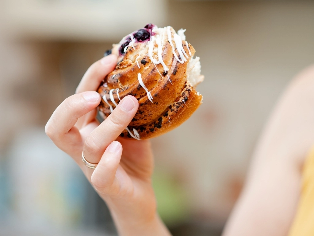 Bitten cinnamon roll in a woman's hand, cozy and sweet moment