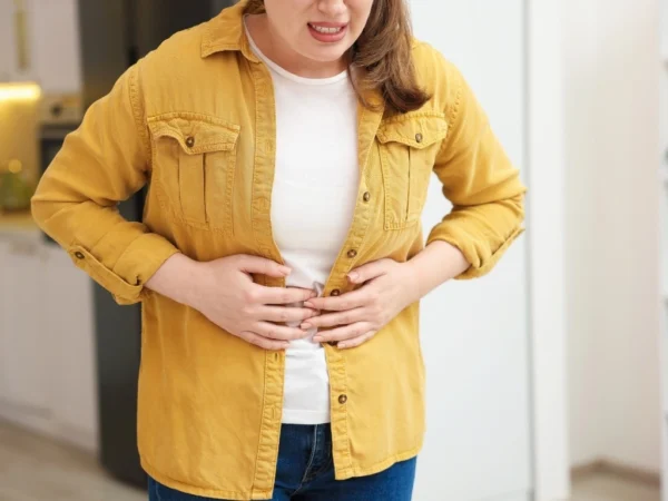 A woman in a yellow jacket holding her stomach, representing IBS-related bloating