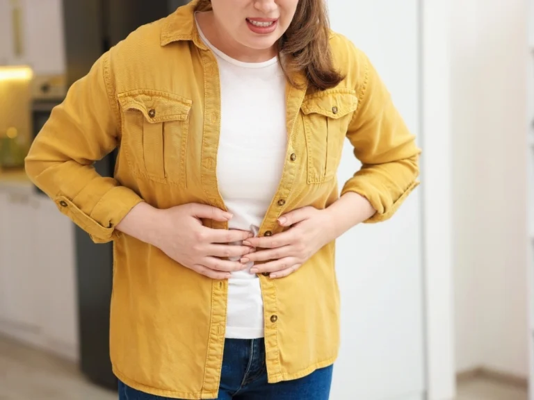A woman in a yellow jacket holding her stomach, representing IBS-related bloating