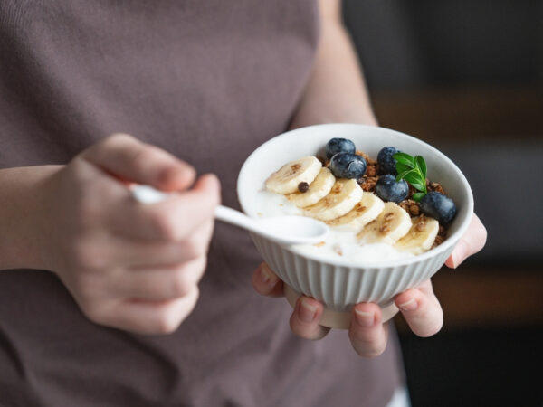 Woman holding a bowl of yogurt topped with slices of banana and berries