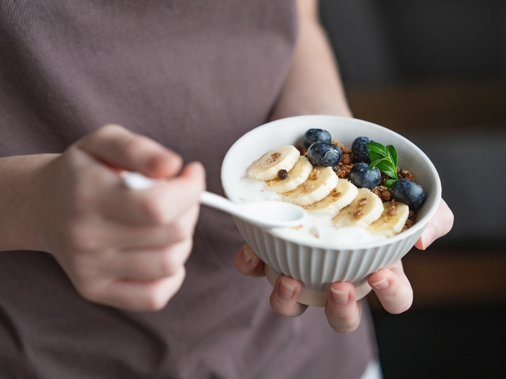 Woman holding a bowl of yogurt topped with slices of banana and berries