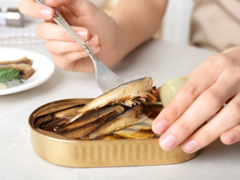 Person scooping canned sardines with a fork