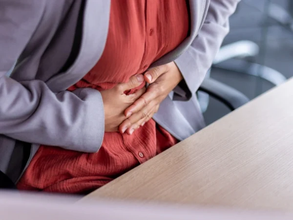 Woman holding her stomach in discomfort while seated at an office desk