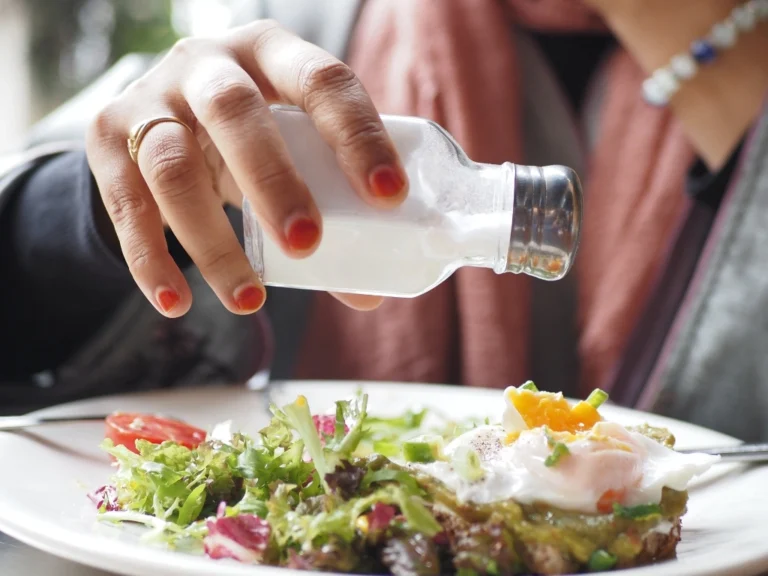 Woman sprinkling salt from a small glass shaker onto a plate of salad
