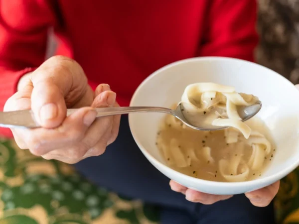 Person scooping noodle soup from a bowl using a spoon