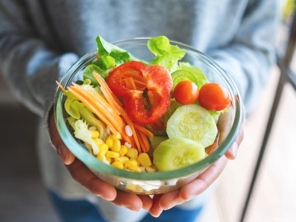 Person holding a bowl of vegetable salad