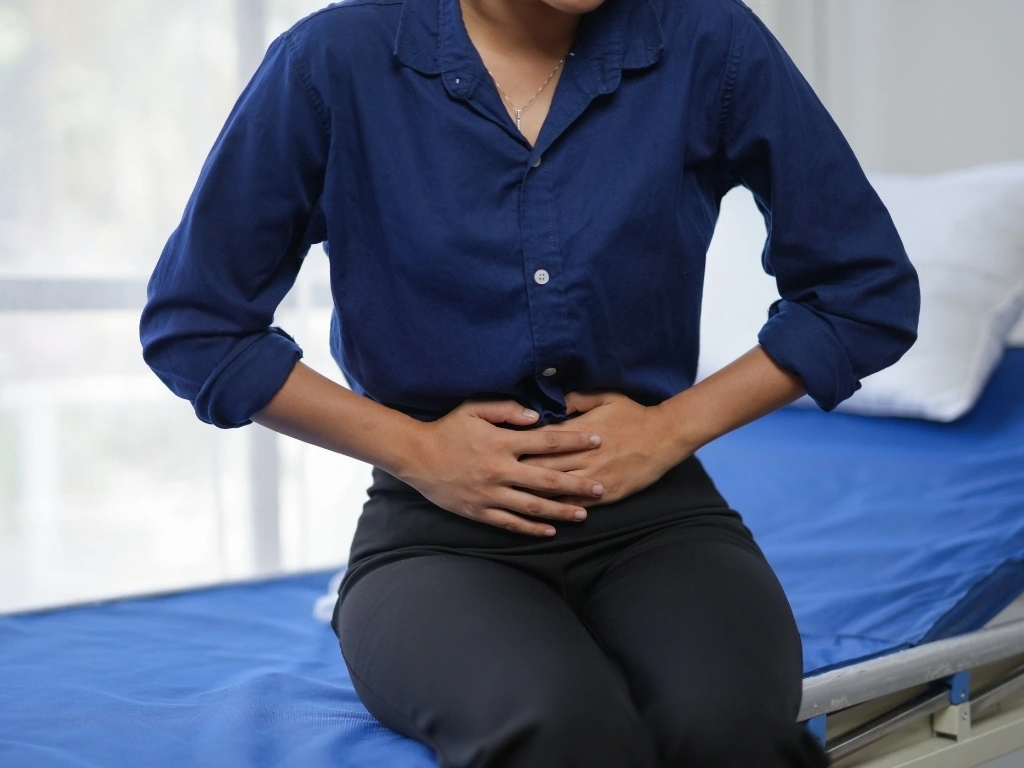 Person experiencing abdominal pain while sitting on a medical examination table