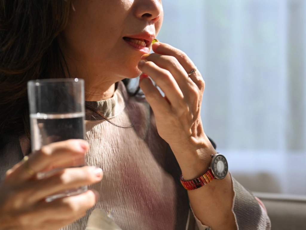 Woman taking antibiotics with a glass of water to treat methane SIBO