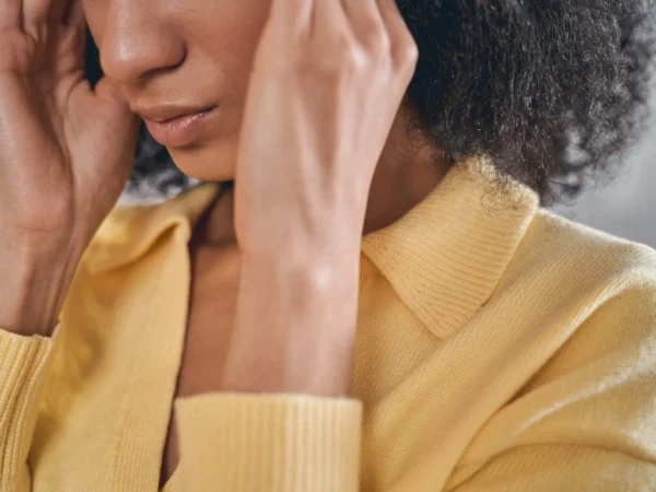 Woman in yellow holding either temple with both hands due to stress