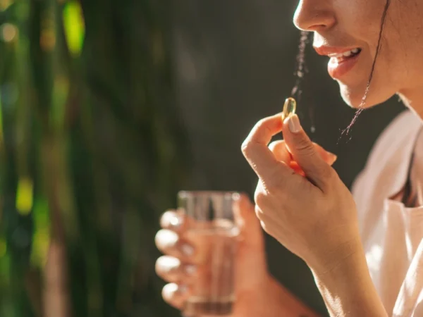 Woman holding a yellow gel capsule and a glass of water in soft sunlight