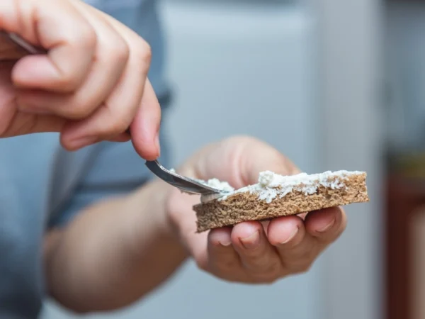 Person spreading cheese on a piece of wheat bread