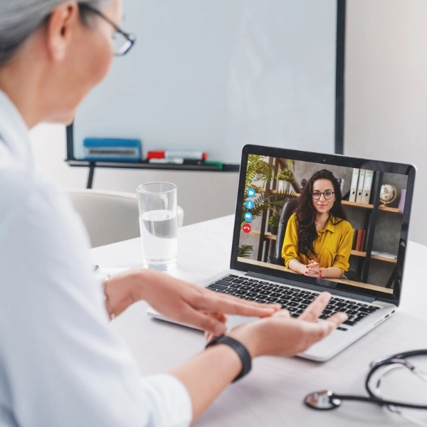Middle-aged doctor talking to a young woman over webcam from the clinic office