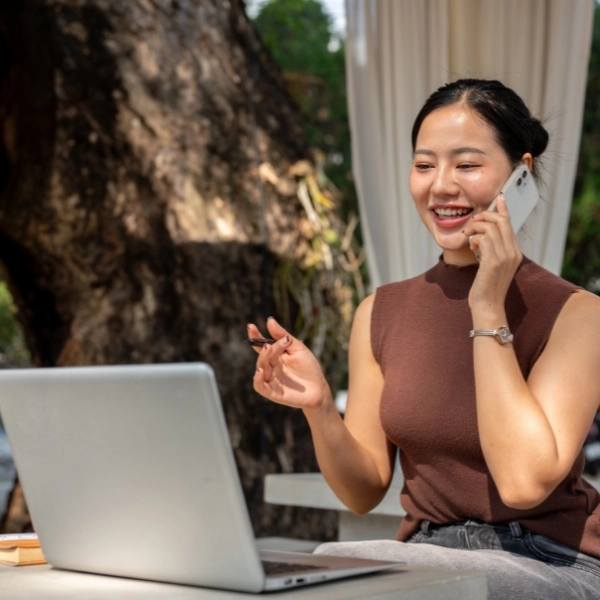 Asian woman talks on the phone with her client while working remotely from a cafe