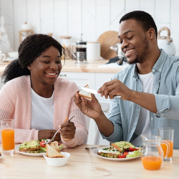 Couple enjoying a healthy breakfast with eggs, vegetables, whole-grain toast, and orange juice at a kitchen table.