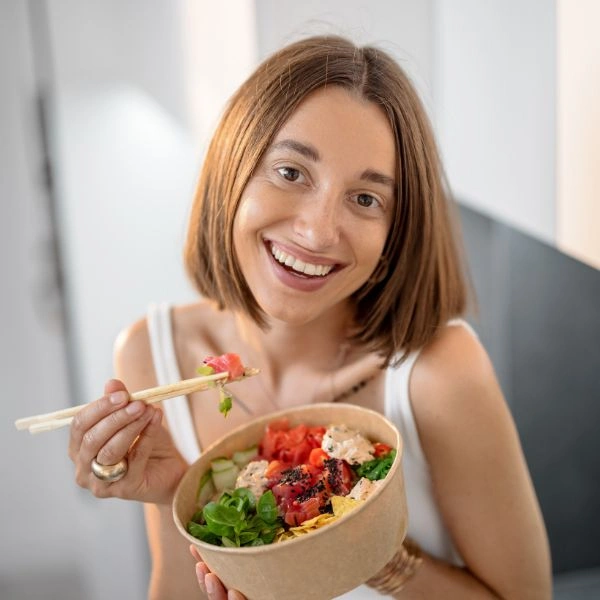 Woman happily eating a healthy meal using chopsticks