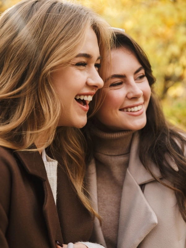 Two cheerful young pretty girls wearing coats walking together