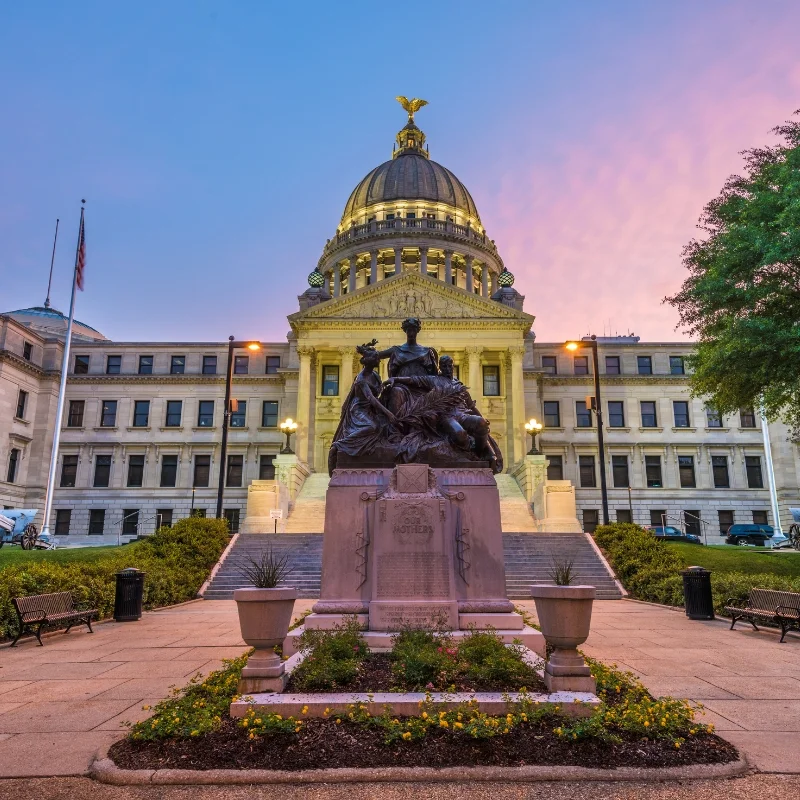 Mississippi State Capitol in Jackson, Mississippi, USA at twilight with the Monument to Women of the Confederacy dating from 1917.