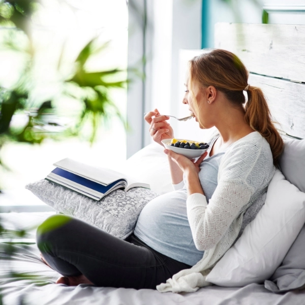 Side view of pregnant woman relaxing at her bedroom and eating