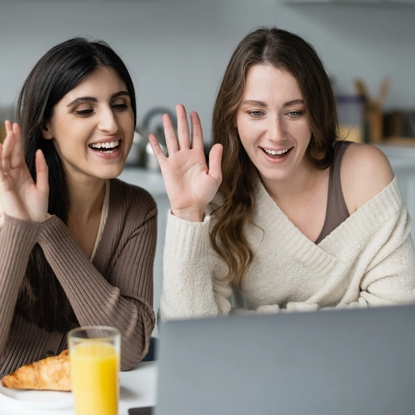 Positive women having video call on laptop near breakfast in kitchen